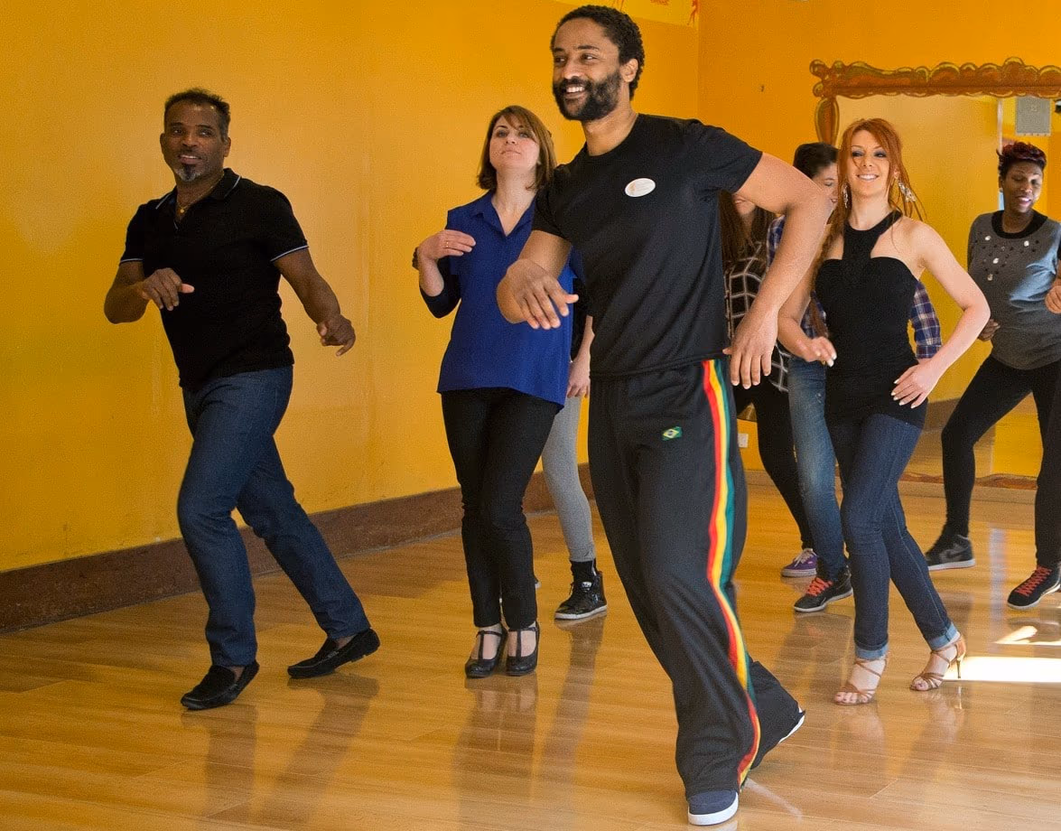 Un groupe danse en ligne dans la salle jaune, mené par un danseur en survêtement.
